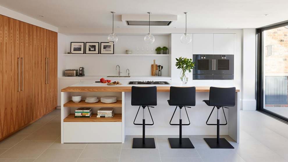 This is an example of a scandinavian kitchen in London with a double-bowl sink, flat-panel cabinets, white cabinets, white splashback, stainless steel appliances, with island, grey floor and white benchtop.