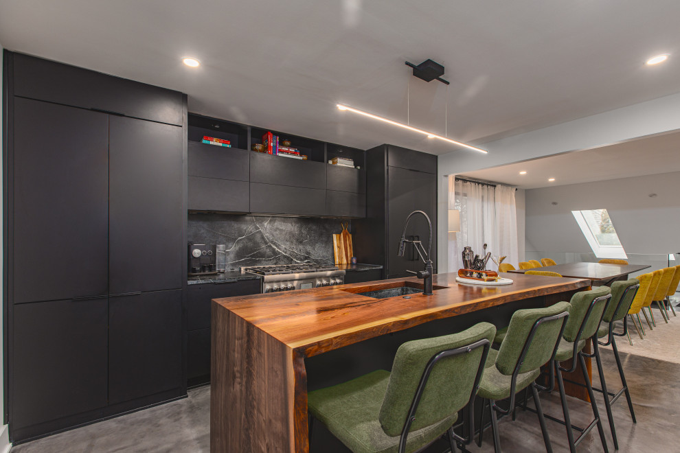 Bild på ett mellanstort industriellt brun brunt kök, med en undermonterad diskho, släta luckor, svarta skåp, svart stänkskydd, stänkskydd i sten, integrerade vitvaror, betonggolv, en köksö, grått golv och träbänkskiva