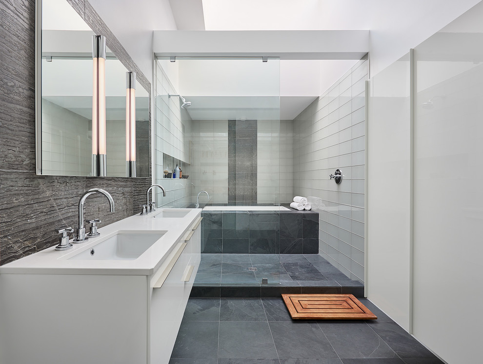 This is an example of a contemporary master bathroom in DC Metro with flat-panel cabinets, white cabinets, a shower/bathtub combo, gray tile, white tile, white walls, porcelain floors, an undermount sink, solid surface benchtops, an undermount tub, glass tile and an open shower.