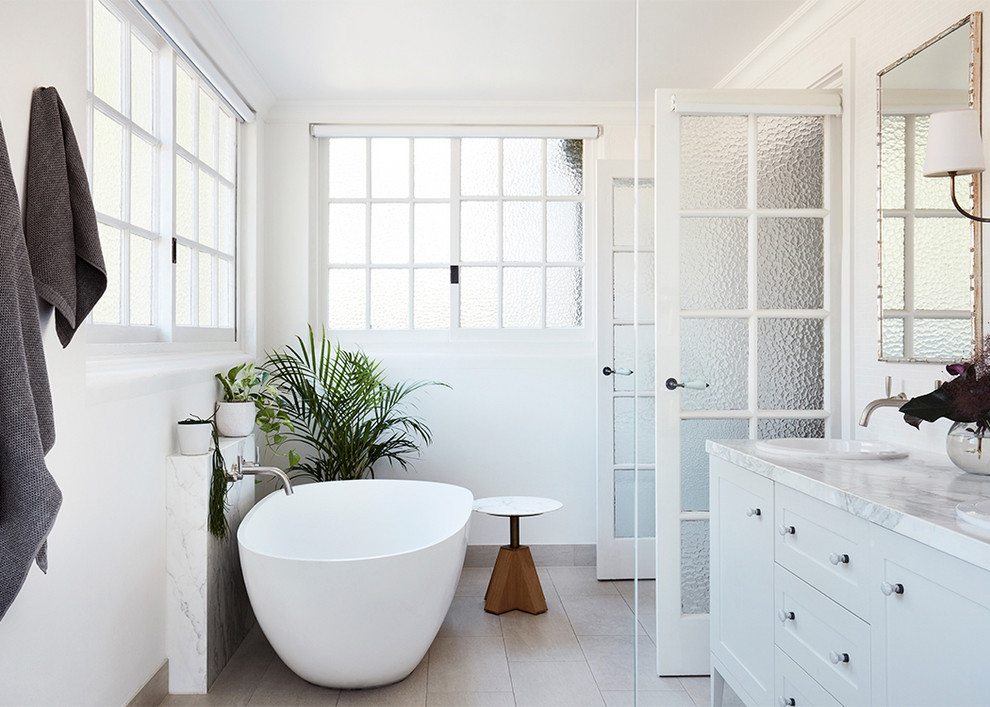 Photo of a transitional bathroom in Sydney with shaker cabinets, white cabinets, a freestanding tub, white walls, a drop-in sink, grey floor and white benchtops.