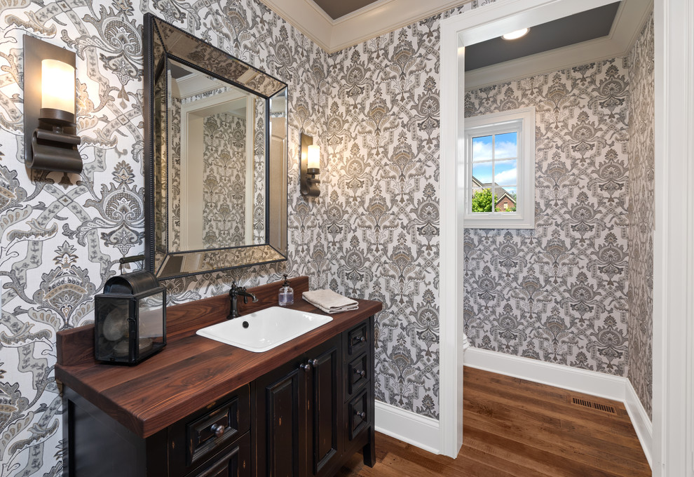 Mid-sized traditional powder room in Cincinnati with furniture-like cabinets, black cabinets, a one-piece toilet, black walls, dark hardwood floors, an undermount sink, wood benchtops, brown floor and brown benchtops.