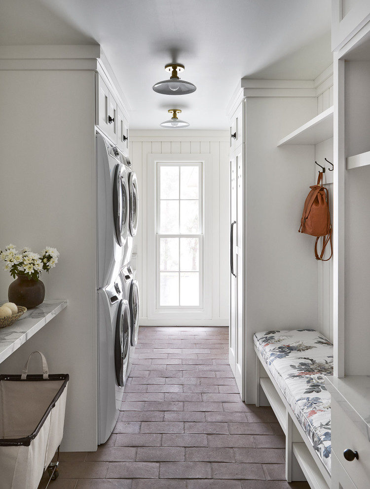 Mid-sized country galley utility room in Chicago with a single-bowl sink, shaker cabinets, white cabinets, white walls, terra-cotta floors, a stacked washer and dryer, brown floor and white benchtop.