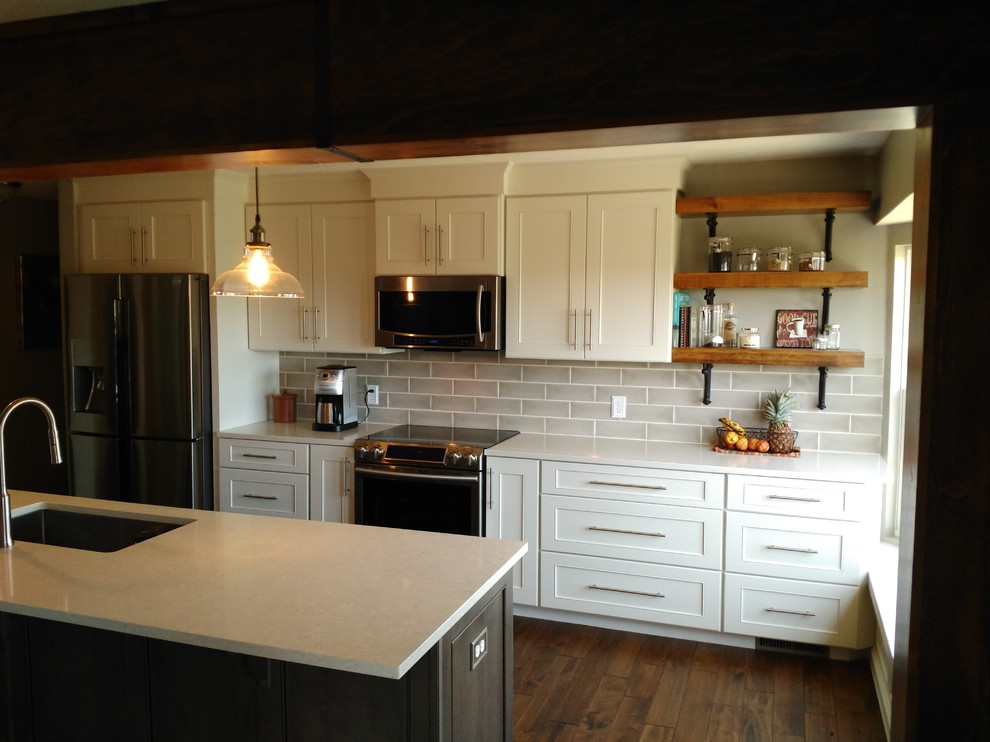 Example of a mid-sized transitional l-shaped dark wood floor and brown floor eat-in kitchen design with a single-bowl sink, shaker cabinets, white cabinets, quartzite countertops, gray backsplash, ceramic backsplash, stainless steel appliances and an island