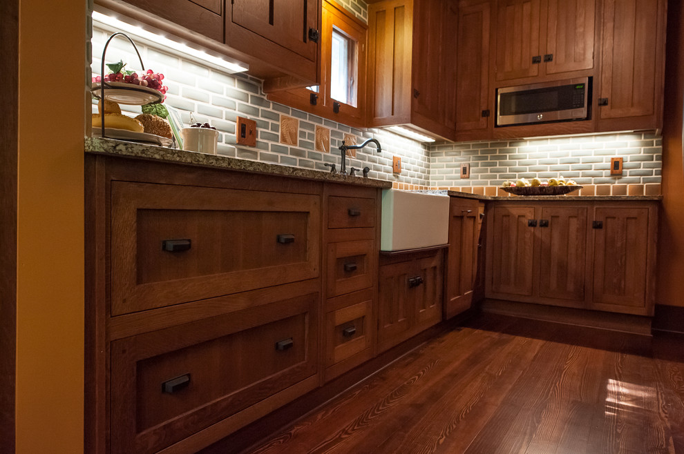 This is an example of a small arts and crafts l-shaped separate kitchen in Detroit with a farmhouse sink, beaded inset cabinets, medium wood cabinets, quartz benchtops, grey splashback, subway tile splashback, stainless steel appliances, dark hardwood floors and no island.