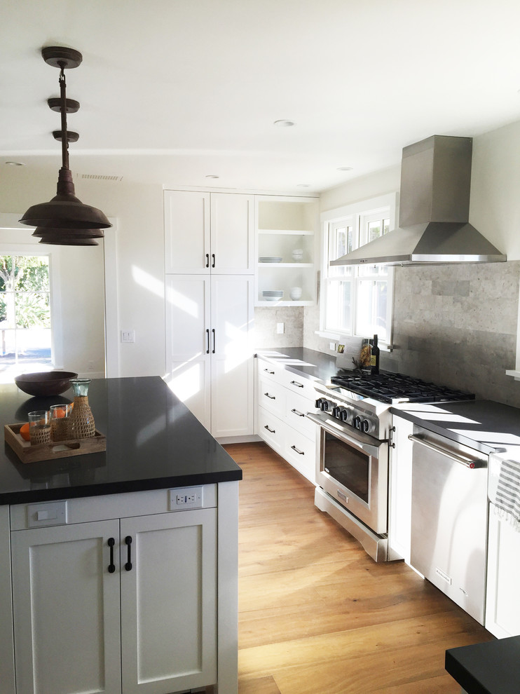 Inspiration for a large country kitchen in Santa Barbara with a farmhouse sink, shaker cabinets, white cabinets, quartz benchtops, grey splashback, stone tile splashback, stainless steel appliances, medium hardwood floors and with island.