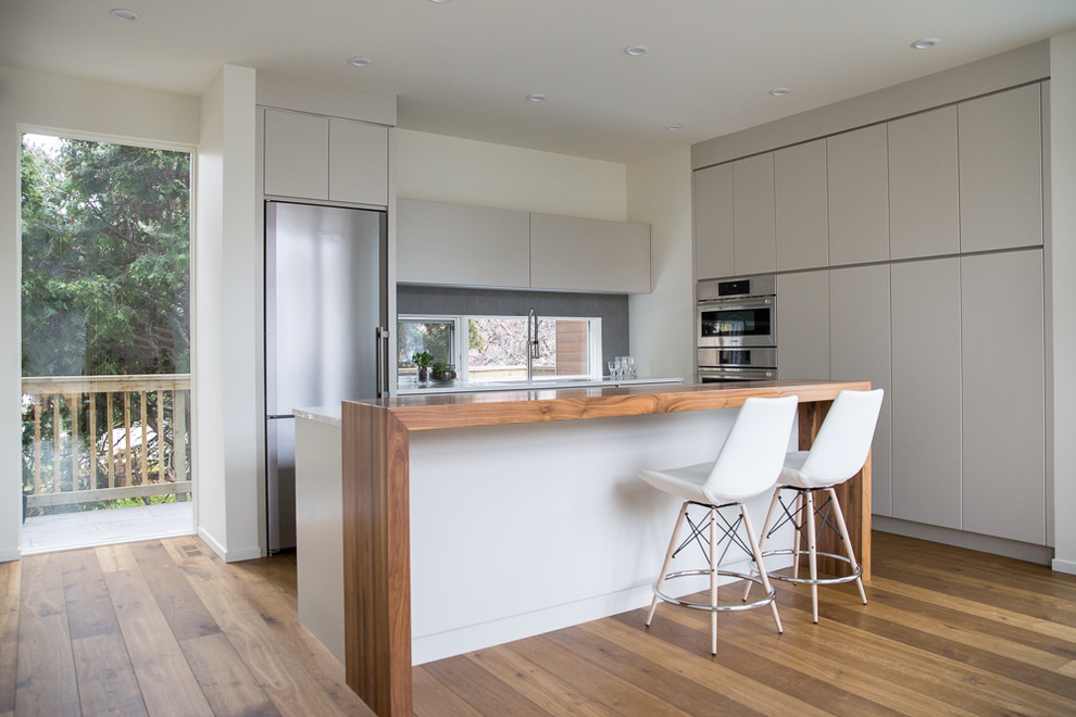 Photo of a mid-sized modern l-shaped eat-in kitchen with an undermount sink, flat-panel cabinets, grey cabinets, quartz benchtops, grey splashback, terra-cotta splashback, stainless steel appliances, medium hardwood floors and with island.