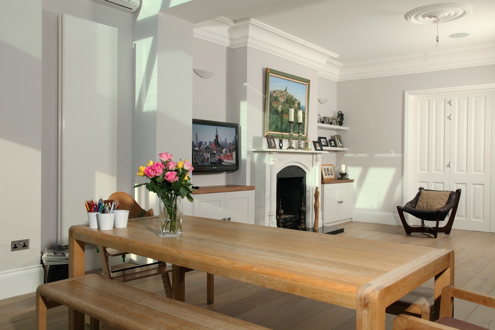This is an example of a mid-sized transitional separate dining room in London with white walls, medium hardwood floors, a standard fireplace and a stone fireplace surround.