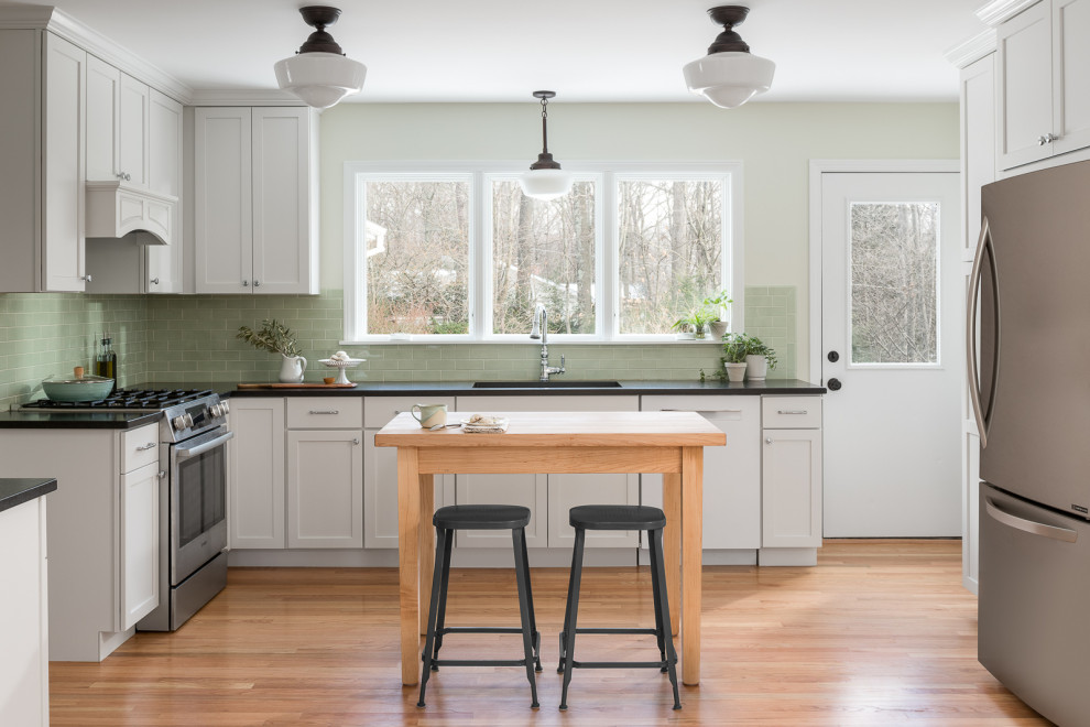Design ideas for a mid-sized traditional l-shaped kitchen in Burlington with an undermount sink, shaker cabinets, white cabinets, quartz benchtops, green splashback, ceramic splashback, stainless steel appliances, light hardwood floors and black benchtop.