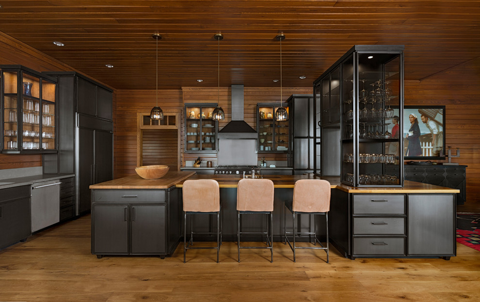 Inspiration for a large country l-shaped open plan kitchen in Detroit with flat-panel cabinets, black cabinets, wood benchtops, stainless steel appliances, medium hardwood floors, with island, brown floor and brown benchtop.