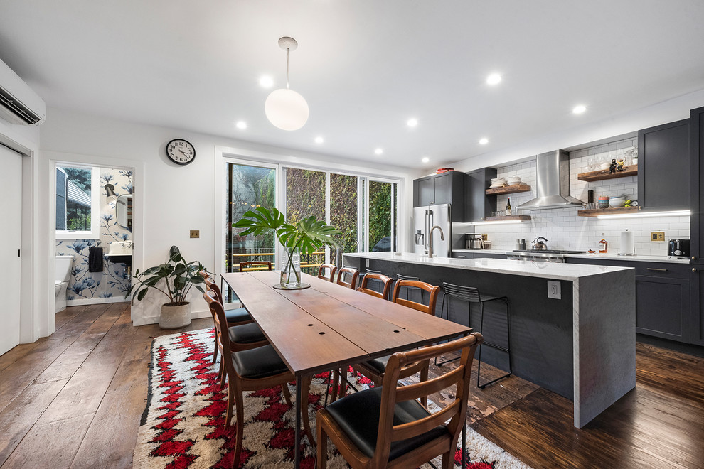 Photo of a contemporary galley eat-in kitchen in New York with shaker cabinets, grey cabinets, white splashback, subway tile splashback, stainless steel appliances, dark hardwood floors, with island, brown floor and grey benchtop.