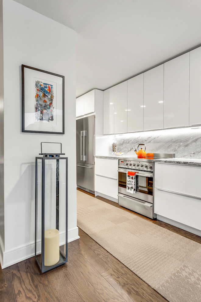 Photo of a mid-sized contemporary l-shaped eat-in kitchen in Chicago with an undermount sink, flat-panel cabinets, white cabinets, granite benchtops, white splashback, marble splashback, stainless steel appliances, medium hardwood floors, with island and white benchtop.