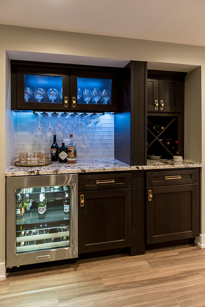 Photo of a mid-sized midcentury single-wall wet bar in Chicago with no sink, shaker cabinets, dark wood cabinets, granite benchtops, grey splashback, subway tile splashback, vinyl floors, brown floor and grey benchtop.