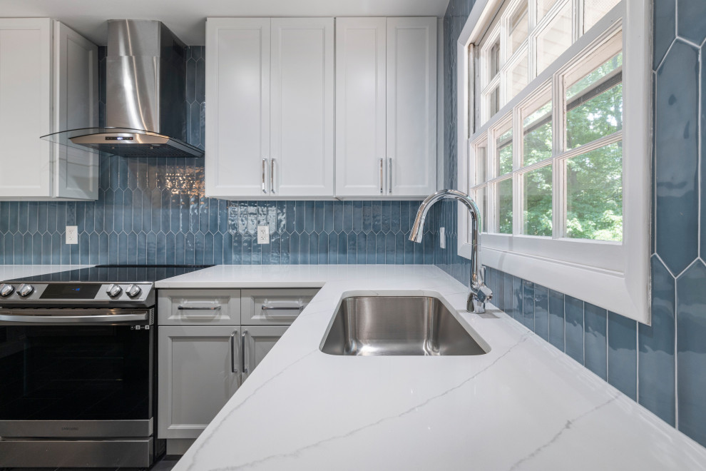 Photo of a large contemporary l-shaped kitchen/diner in DC Metro with shaker cabinets, white cabinets, engineered stone countertops, blue splashback, ceramic splashback, porcelain flooring, grey floors, white worktops, a submerged sink, stainless steel appliances and a breakfast bar.