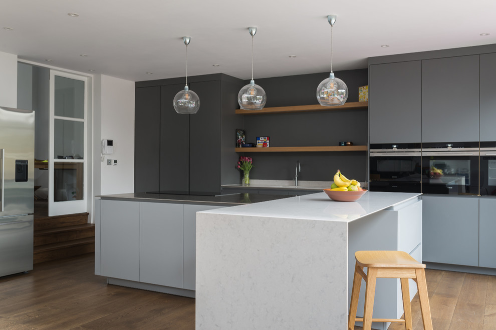 Design ideas for a large contemporary kitchen in London with flat-panel cabinets, grey cabinets, stainless steel benchtops, multiple islands, grey splashback, black appliances and light hardwood floors.