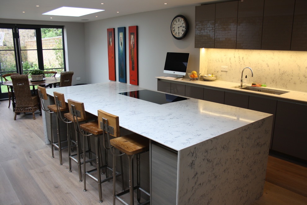 Large contemporary galley eat-in kitchen in London with an undermount sink, flat-panel cabinets, brown cabinets, solid surface benchtops, grey splashback, stainless steel appliances, light hardwood floors, with island and stone slab splashback.