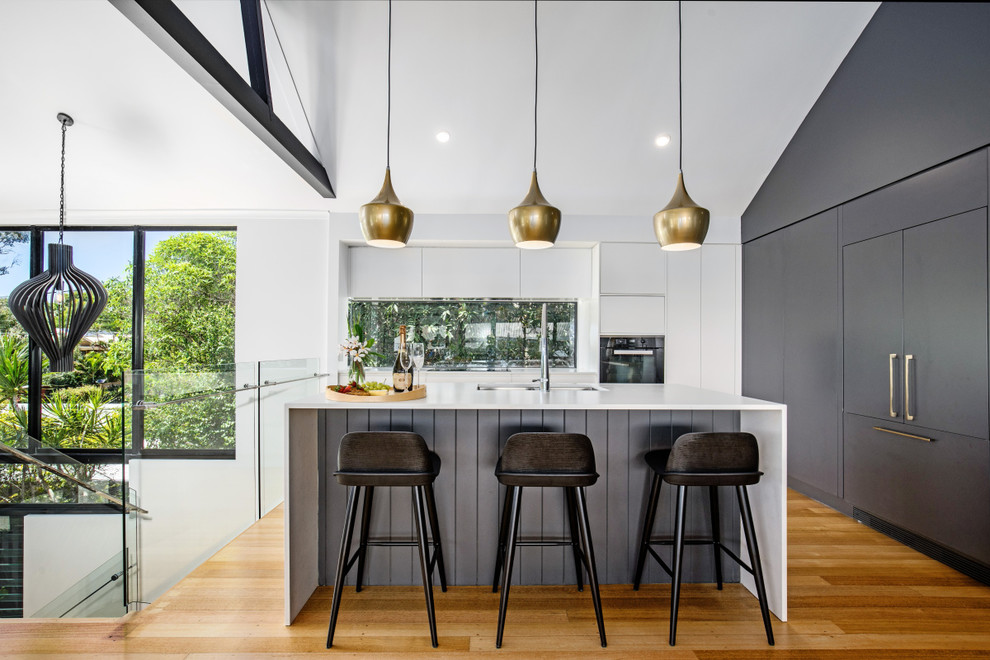 Mid-sized contemporary l-shaped open plan kitchen in Sunshine Coast with an undermount sink, flat-panel cabinets, quartz benchtops, window splashback, with island, white benchtop, white cabinets, panelled appliances, medium hardwood floors and brown floor.