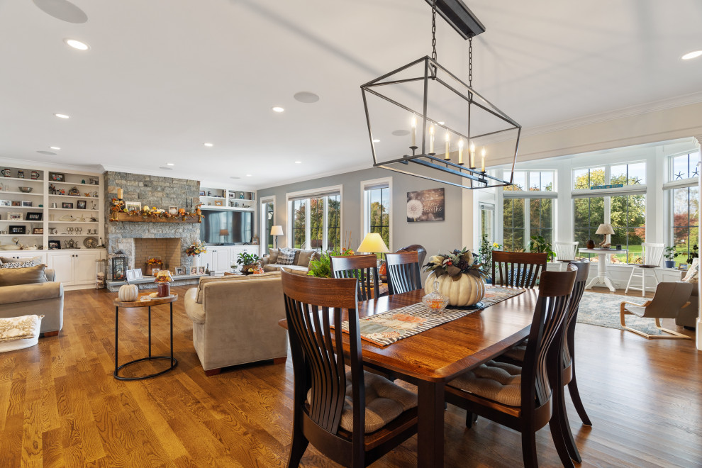 Foto di una sala da pranzo aperta verso la cucina country di medie dimensioni con pareti grigie, pavimento in legno massello medio, camino classico e pavimento marrone