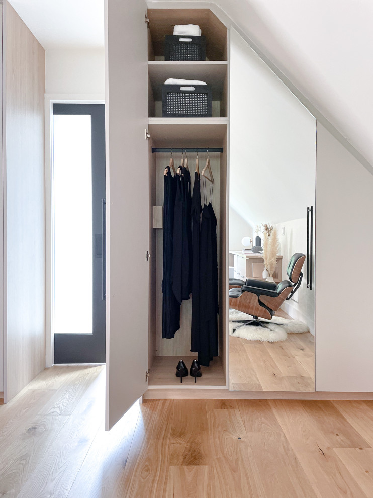 Design ideas for a small modern gender neutral built-in wardrobe in Toronto with flat-panel cabinets, beige cabinets, light hardwood flooring, beige floors and a vaulted ceiling.