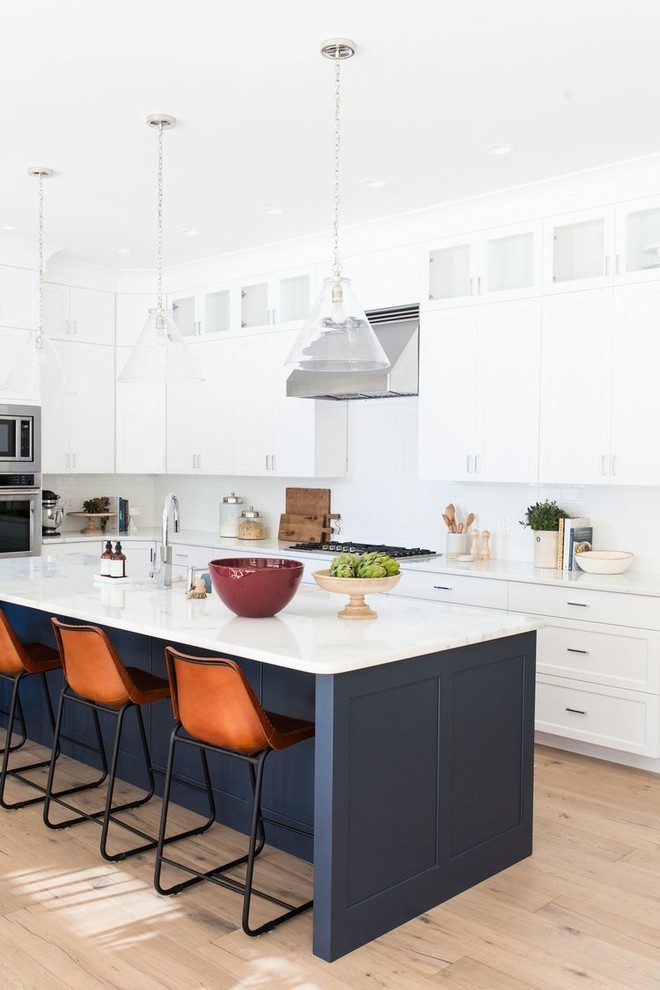 This is an example of a mid-sized beach style galley eat-in kitchen in Salt Lake City with a drop-in sink, white cabinets, white splashback, subway tile splashback, light hardwood floors and with island.