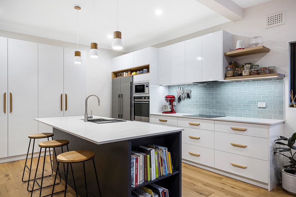 Design ideas for a mid-sized modern l-shaped open plan kitchen in Sydney with an undermount sink, flat-panel cabinets, white cabinets, quartz benchtops, green splashback, subway tile splashback, stainless steel appliances, light hardwood floors, with island, brown floor and white benchtop.