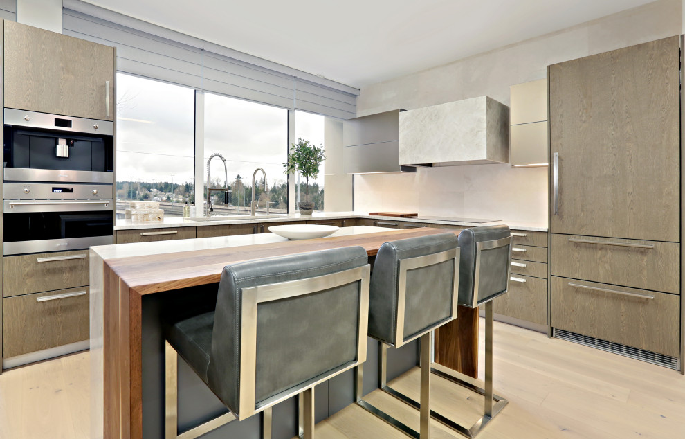 Open concept kitchen - mid-sized transitional l-shaped light wood floor and beige floor open concept kitchen idea in Seattle with an undermount sink, flat-panel cabinets, gray cabinets, quartzite countertops, beige backsplash, limestone backsplash, stainless steel appliances, an island and beige countertops