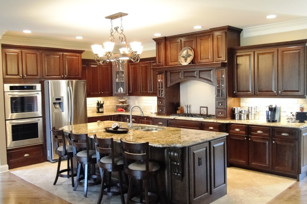Example of a large transitional l-shaped travertine floor open concept kitchen design with an undermount sink, raised-panel cabinets, dark wood cabinets, granite countertops, beige backsplash, subway tile backsplash, stainless steel appliances and an island
