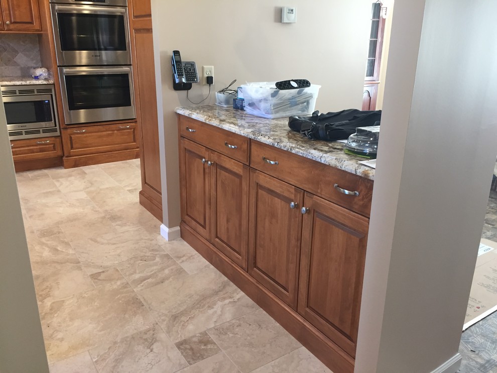 Mid-sized traditional l-shaped separate kitchen in Baltimore with an undermount sink, raised-panel cabinets, medium wood cabinets, granite benchtops, beige splashback, travertine splashback, stainless steel appliances, porcelain floors, no island and beige floor.