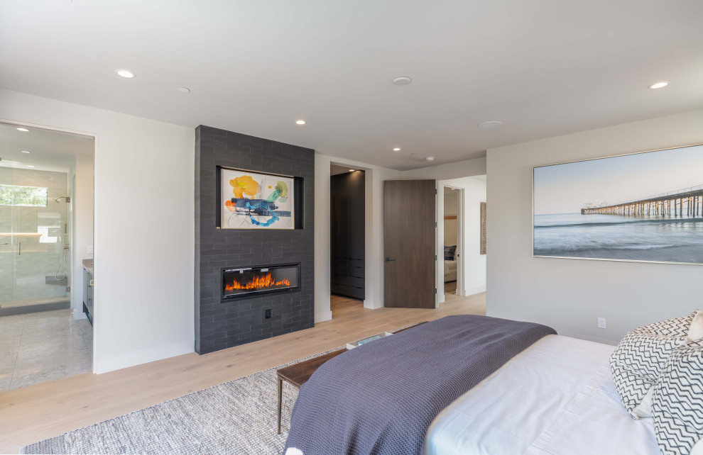 Photo of a large modern master bedroom in Los Angeles with white walls, light hardwood floors, a ribbon fireplace, a tile fireplace surround, beige floor and wallpaper.