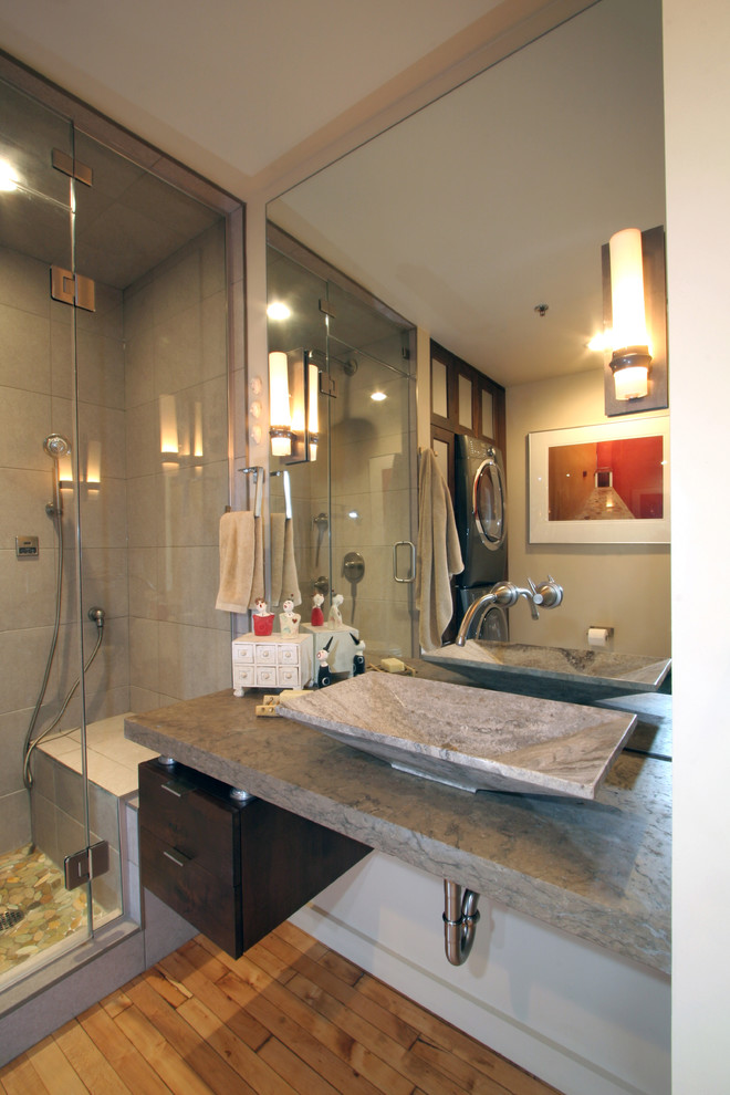 Photo of a small industrial master bathroom in Milwaukee with a vessel sink, flat-panel cabinets, dark wood cabinets, limestone benchtops, an alcove shower, gray tile, stone tile, white walls and light hardwood floors.