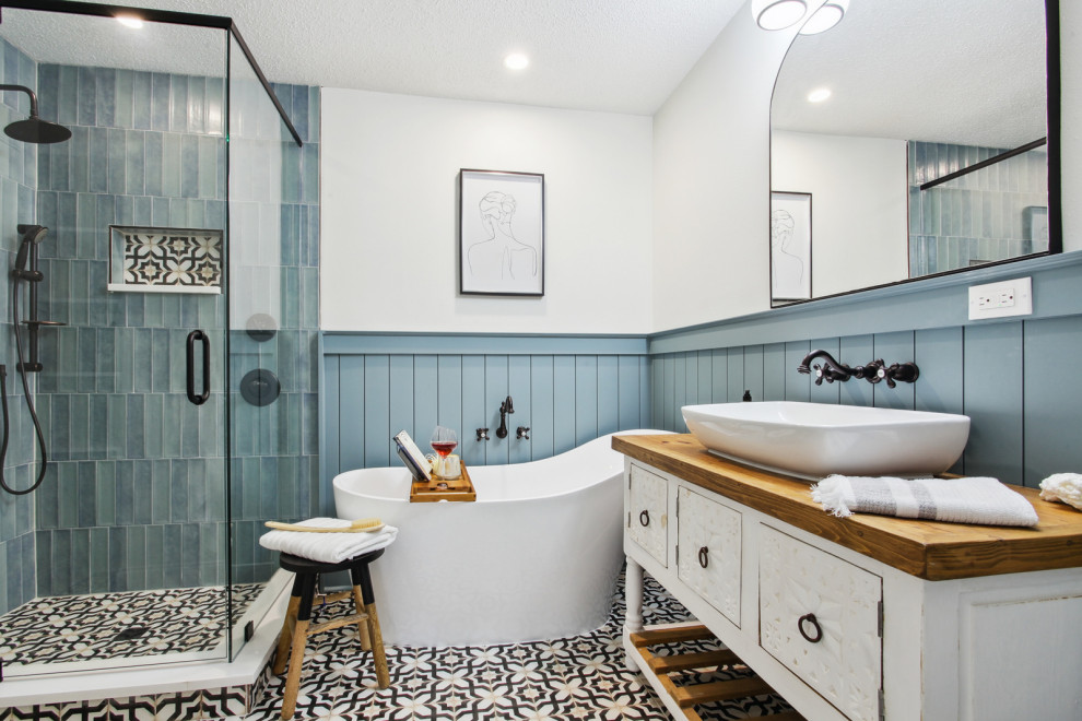 Свежая идея для дизайна: главная ванная комната среднего размера с фасадами островного типа, искусственно-состаренными фасадами, отдельно стоящей ванной, угловым душем, раздельным унитазом, синей плиткой, керамической плиткой, синими стенами, полом из керамической плитки, настольной раковиной, столешницей из дерева, черным полом, душем с распашными дверями, коричневой столешницей, нишей, тумбой под одну раковину, напольной тумбой и стенами из вагонки - отличное фото интерьера