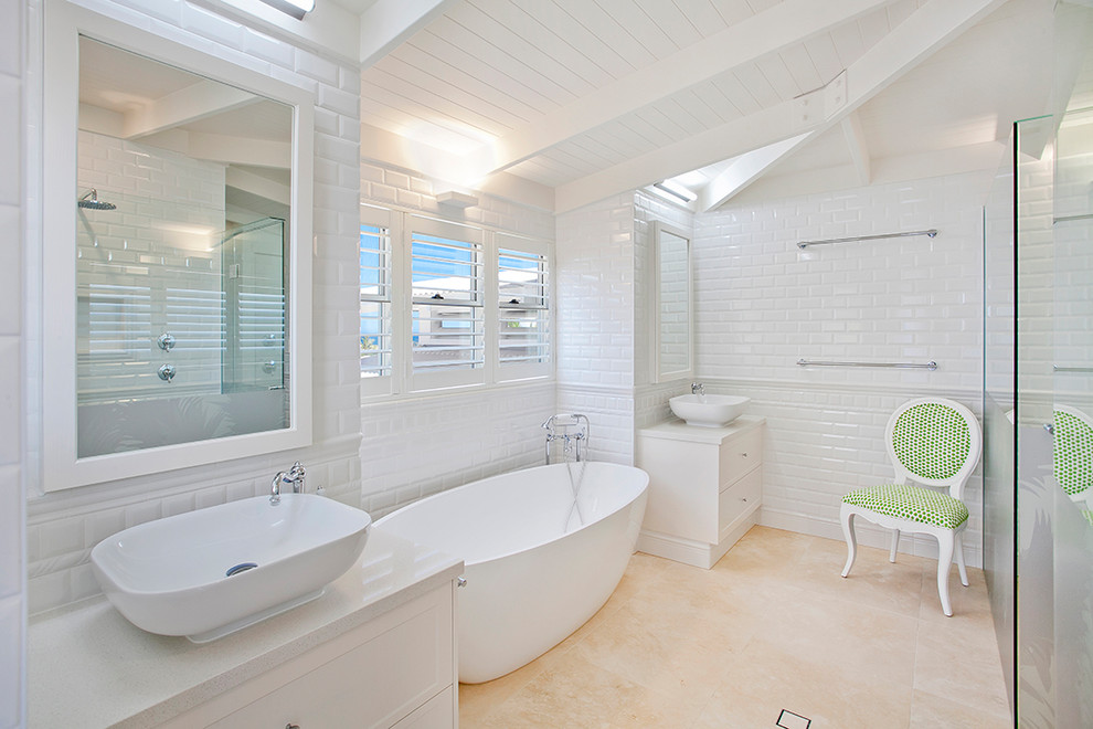 Large beach style master bathroom in Sunshine Coast with recessed-panel cabinets, white cabinets, a freestanding tub, a double shower, a two-piece toilet, white tile, subway tile, white walls, porcelain floors, a vessel sink, beige floor and a hinged shower door.