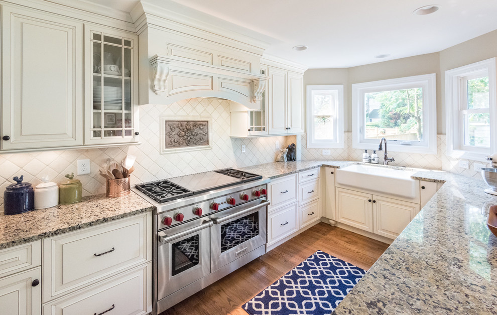 Transitional medium tone wood floor kitchen photo in Richmond with a farmhouse sink, raised-panel cabinets, granite countertops, beige backsplash, stone tile backsplash, stainless steel appliances, white cabinets and a peninsula