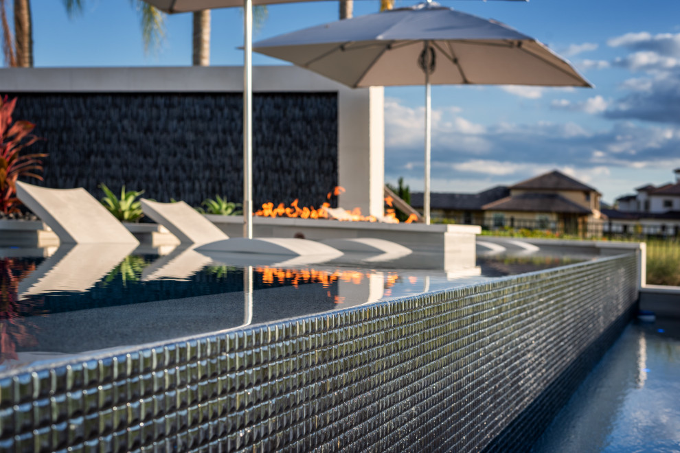 Ispirazione per un'ampia piscina a sfioro infinito minimalista personalizzata dietro casa con paesaggistica bordo piscina e piastrelle