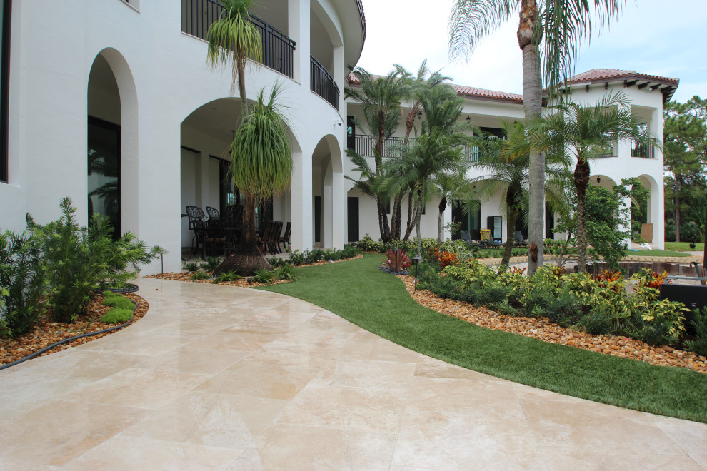 This is an example of an expansive tropical backyard partial sun xeriscape in Miami with a retaining wall and natural stone pavers.
