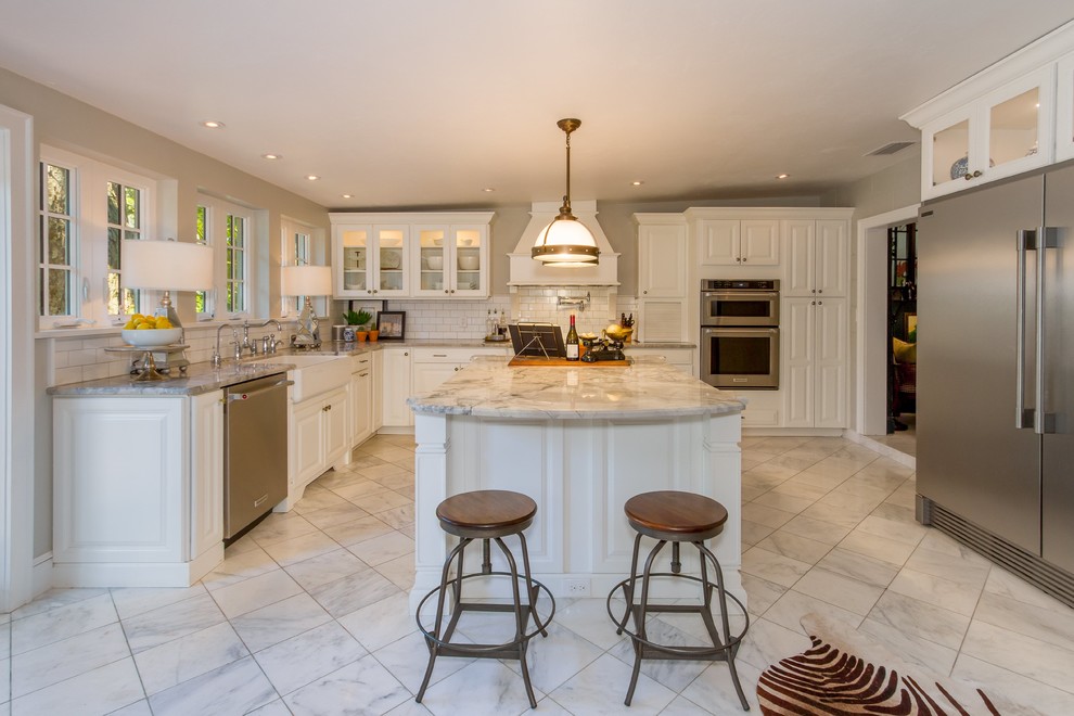 Example of a mid-sized transitional u-shaped porcelain tile and white floor open concept kitchen design in Miami with a farmhouse sink, raised-panel cabinets, white cabinets, marble countertops, white backsplash, subway tile backsplash, stainless steel appliances and an island