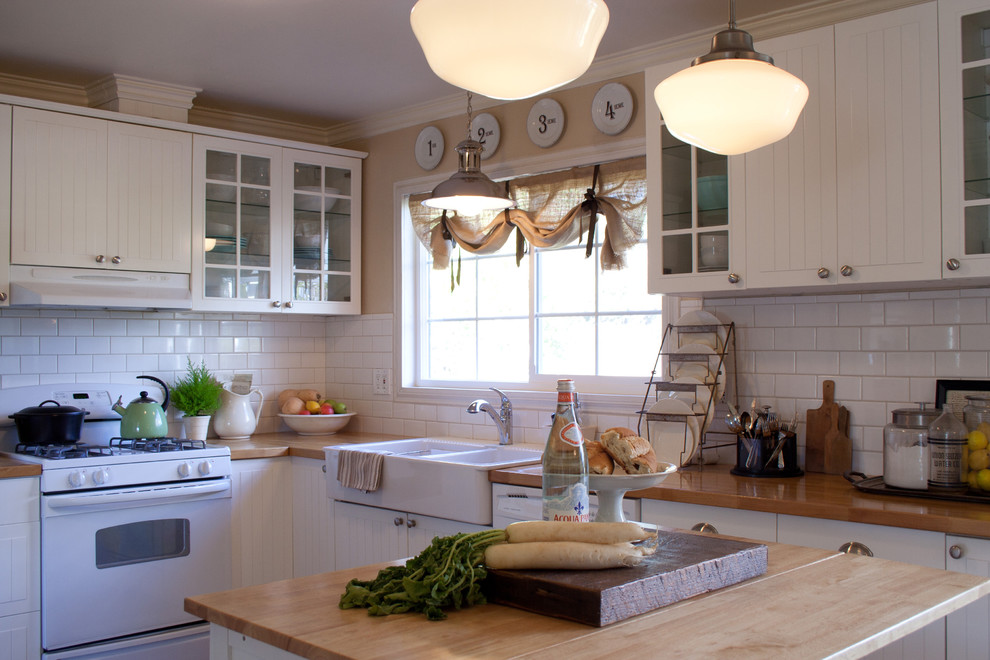 Inspiration for a mid-sized traditional l-shaped eat-in kitchen in Los Angeles with subway tile splashback, a farmhouse sink, wood benchtops, glass-front cabinets, white cabinets, white splashback, white appliances, with island and vinyl floors.