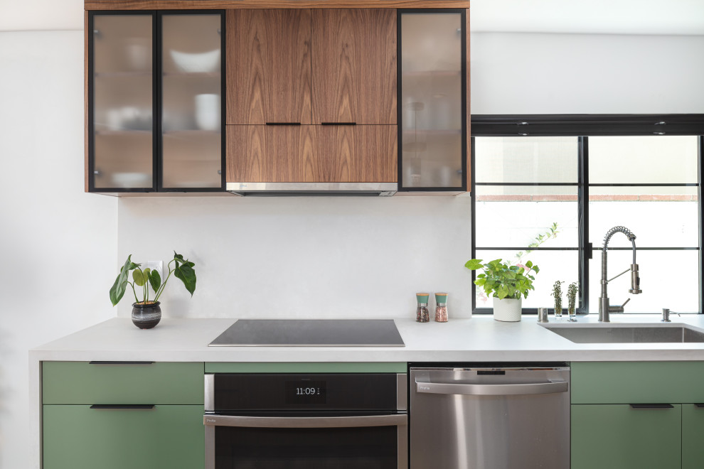 This is an example of a small contemporary galley open plan kitchen in Los Angeles with an undermount sink, flat-panel cabinets, green cabinets, quartz benchtops, white splashback, engineered quartz splashback, stainless steel appliances, light hardwood floors, a peninsula, brown floor and white benchtop.