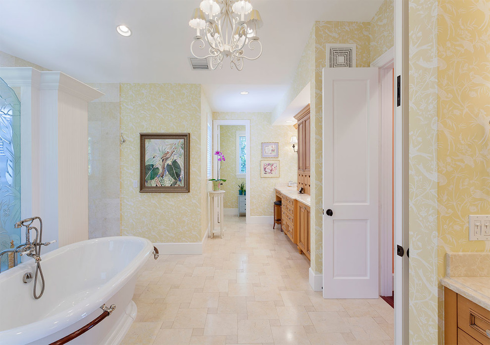 Mid-sized tropical master bathroom in Other with recessed-panel cabinets, medium wood cabinets, a freestanding tub, an open shower, a one-piece toilet, yellow walls, porcelain floors, an undermount sink, marble benchtops, beige floor, an open shower and beige benchtops.