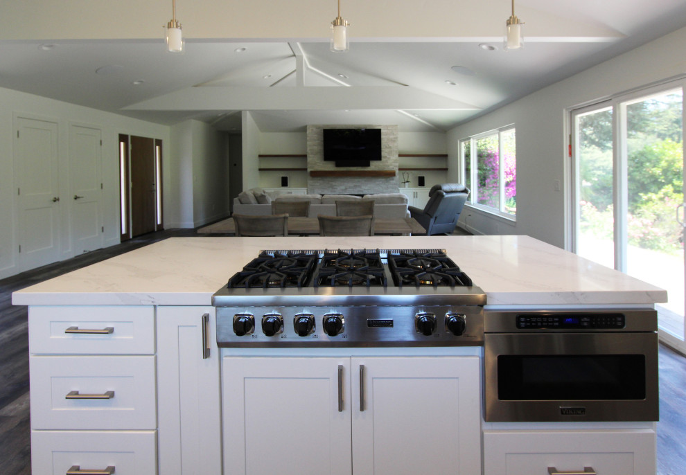 Open concept kitchen - large transitional single-wall vinyl floor and brown floor open concept kitchen idea with an undermount sink, shaker cabinets, white cabinets, quartz countertops, gray backsplash, ceramic backsplash, stainless steel appliances, an island and white countertops