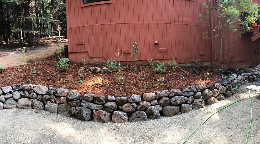 Photo of a large country side yard partial sun xeriscape for spring in Sacramento with a retaining wall and gravel.