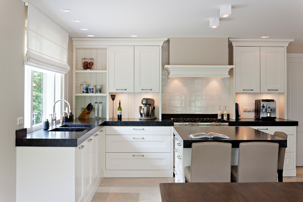 Photo of a transitional l-shaped kitchen in New York with a double-bowl sink, recessed-panel cabinets, white cabinets and white splashback.