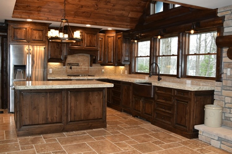 Example of a mid-sized mountain style l-shaped travertine floor and brown floor enclosed kitchen design in Chicago with a farmhouse sink, raised-panel cabinets, dark wood cabinets, granite countertops, stainless steel appliances, an island and white countertops