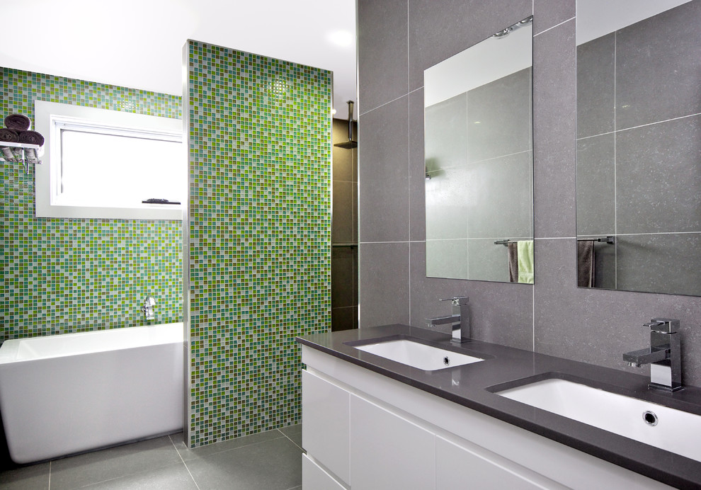 Photo of a mid-sized contemporary bathroom in Other with flat-panel cabinets, white cabinets, a freestanding tub, an open shower, green tile, gray tile, mosaic tile, multi-coloured walls, ceramic floors, a drop-in sink and granite benchtops.