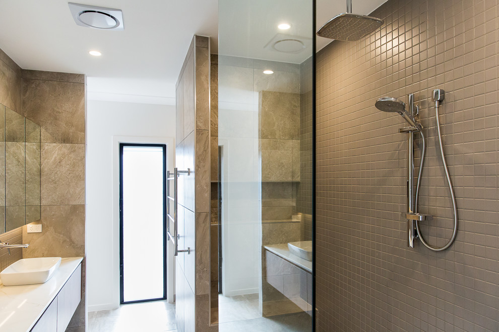This is an example of a contemporary master bathroom in Townsville with flat-panel cabinets, dark wood cabinets, a curbless shower, brown tile, mosaic tile, white walls, ceramic floors, a vessel sink, marble benchtops, grey floor and an open shower.