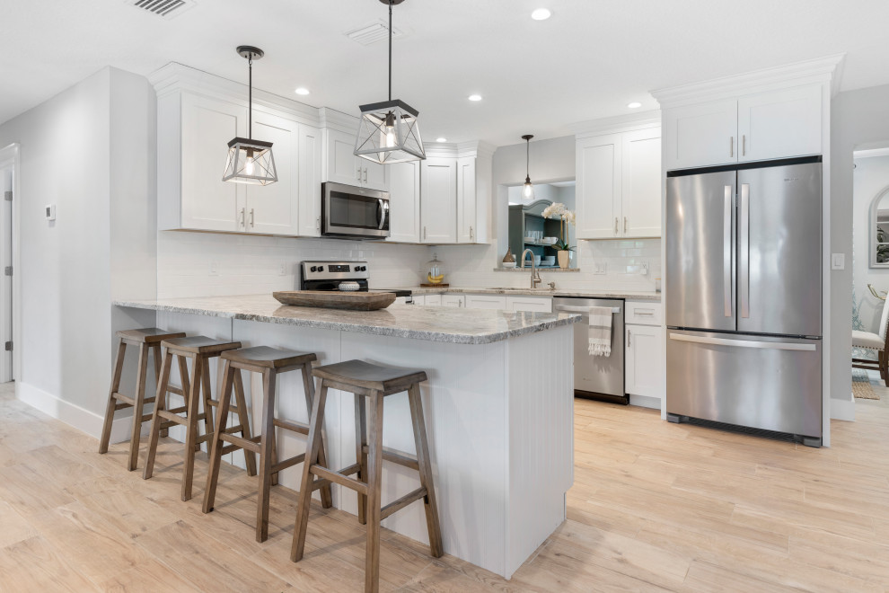 This is an example of a small beach style u-shaped eat-in kitchen in Orlando with a drop-in sink, shaker cabinets, white cabinets, quartz benchtops, white splashback, ceramic splashback, stainless steel appliances, porcelain floors, beige floor and multi-coloured benchtop.