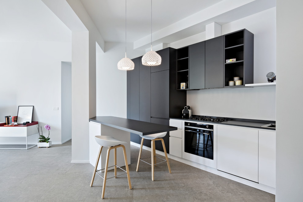 Design ideas for a contemporary open plan kitchen in Milan with flat-panel cabinets, black cabinets, black appliances, a peninsula, a drop-in sink, laminate benchtops, porcelain floors, grey floor and black benchtop.