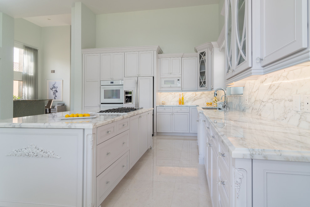 Large traditional l-shaped open plan kitchen in Miami with an undermount sink, recessed-panel cabinets, white cabinets, marble benchtops, multi-coloured splashback, stone slab splashback, stainless steel appliances, porcelain floors and with island.