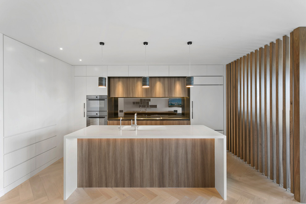 Photo of a mid-sized contemporary l-shaped open plan kitchen in Sydney with an integrated sink, medium wood cabinets, solid surface benchtops, mirror splashback and light hardwood floors.