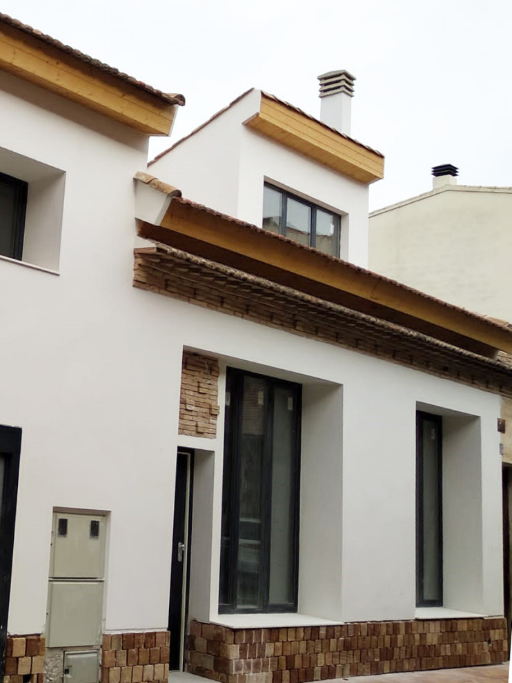 Idée de décoration pour une façade de maison méditerranéenne en stuc à un étage avec un toit papillon et un toit en tuile.