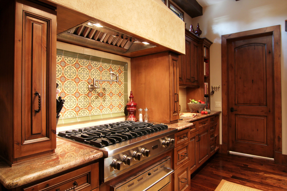 Design ideas for a mid-sized mediterranean galley eat-in kitchen in Houston with a double-bowl sink, raised-panel cabinets, dark wood cabinets, wood benchtops, multi-coloured splashback, terra-cotta splashback, stainless steel appliances, dark hardwood floors and with island.